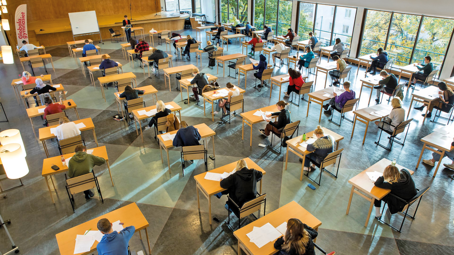 Elever skriver prov i stor sal med stora fönster